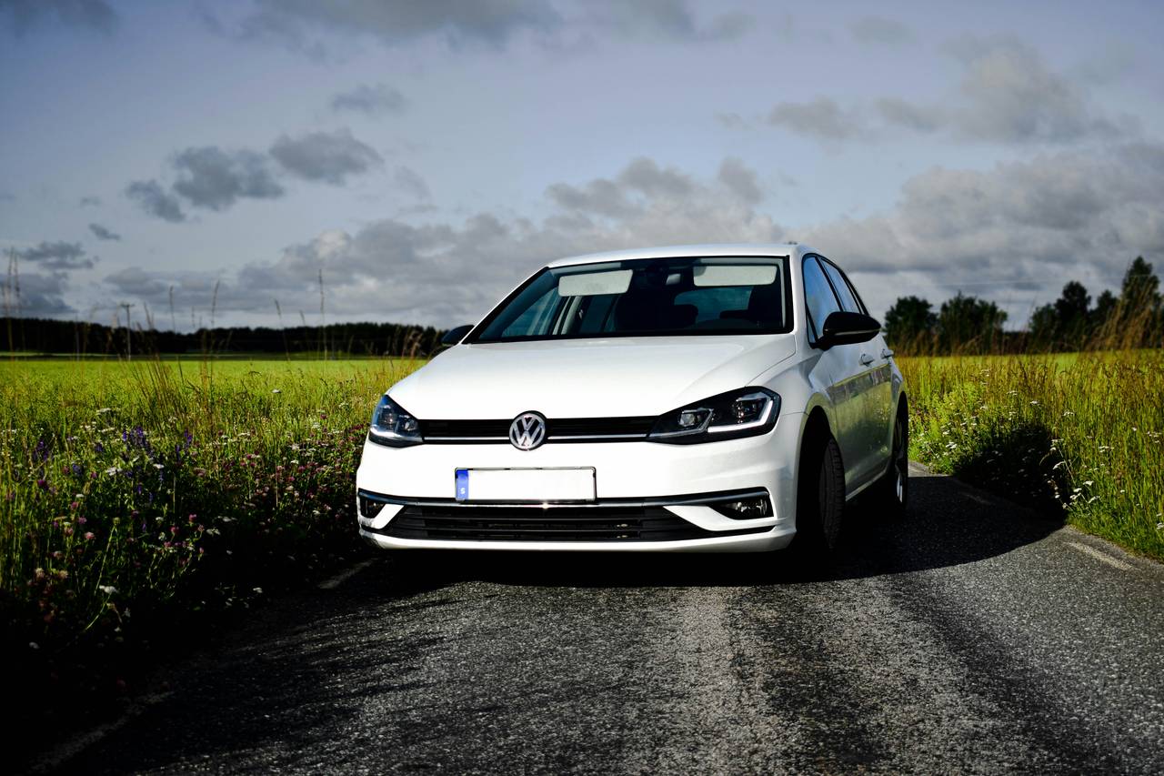 Weisser VW Golf, schräg von vorne, auf einer Landstrasse zwischen Wiesen