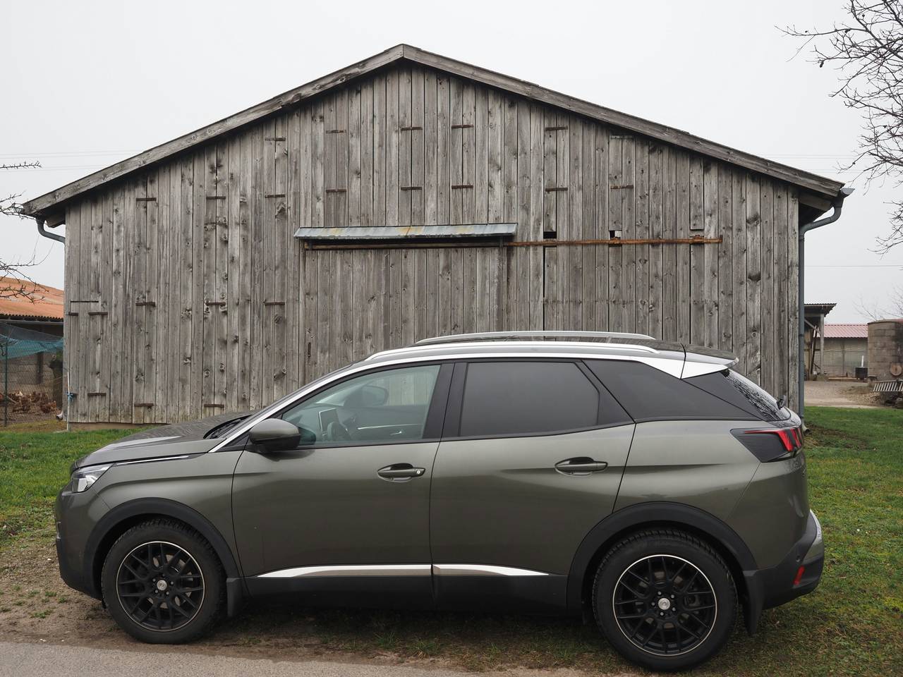 Grauer Peugeot 3008 von der Seite vor einer alten Holzscheune