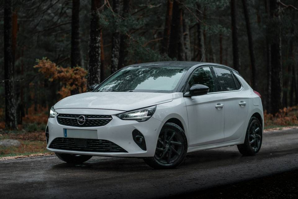 Weisser Opel Corsa, schräg von vorne, an einem Waldrand