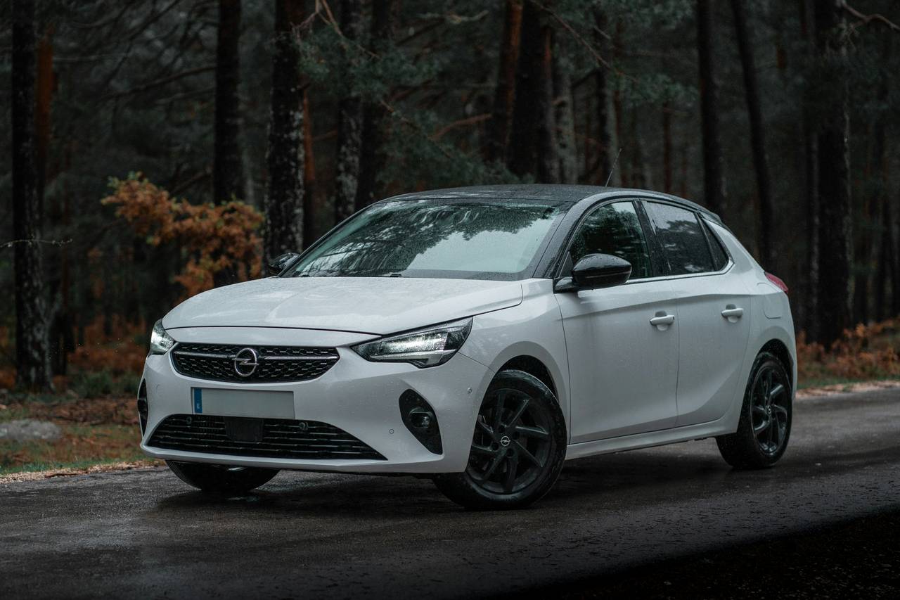 Weisser Opel Corsa, schräg von vorne, an einem Waldrand
