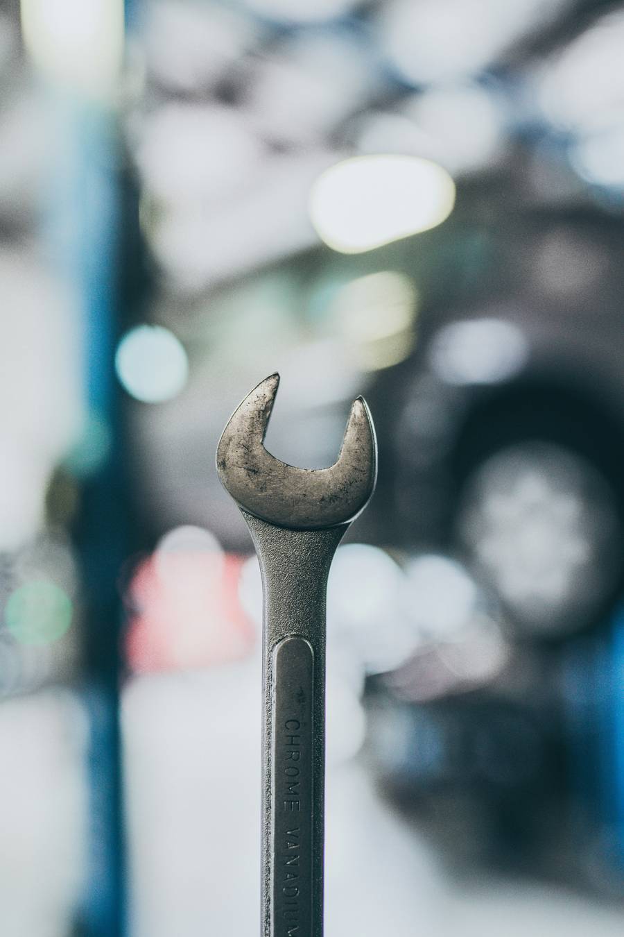 Ein abgenutzter Gabelschlüssel vor einer unscharfen Werkstatt mit Auto auf der Hebebühne