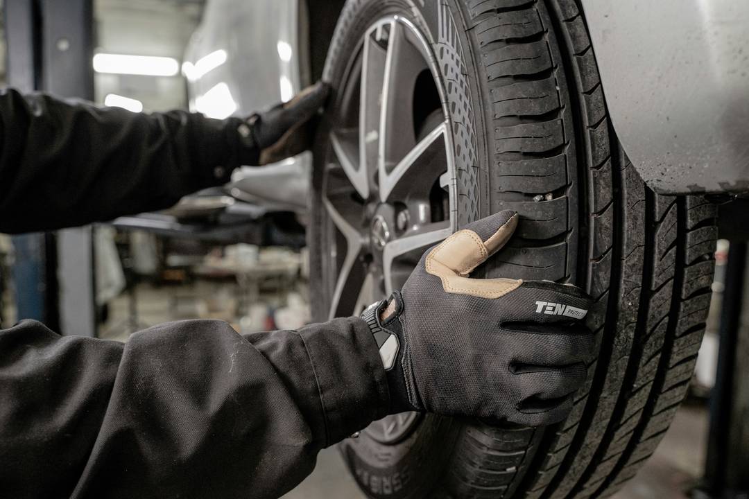Ein Mechaniker in Arbeitshandschuhen montiert ein Rad an einem Auto